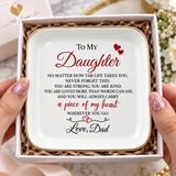 A square white ceramic keepsake dish with rounded corners, gold trim, and a sentimental quote for a daughter, held in a gift box by two hands. The quote is printed in black and red text with small red hearts.
