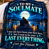 A dark blue fleece blanket draped over a bed, featuring a printed graphic of a couple sitting by a lake at night under a full moon, with the text 'TO MY SOULMATE I may not have been your first love, but I want to be your LAST EVERYTHING. Love You Forever.