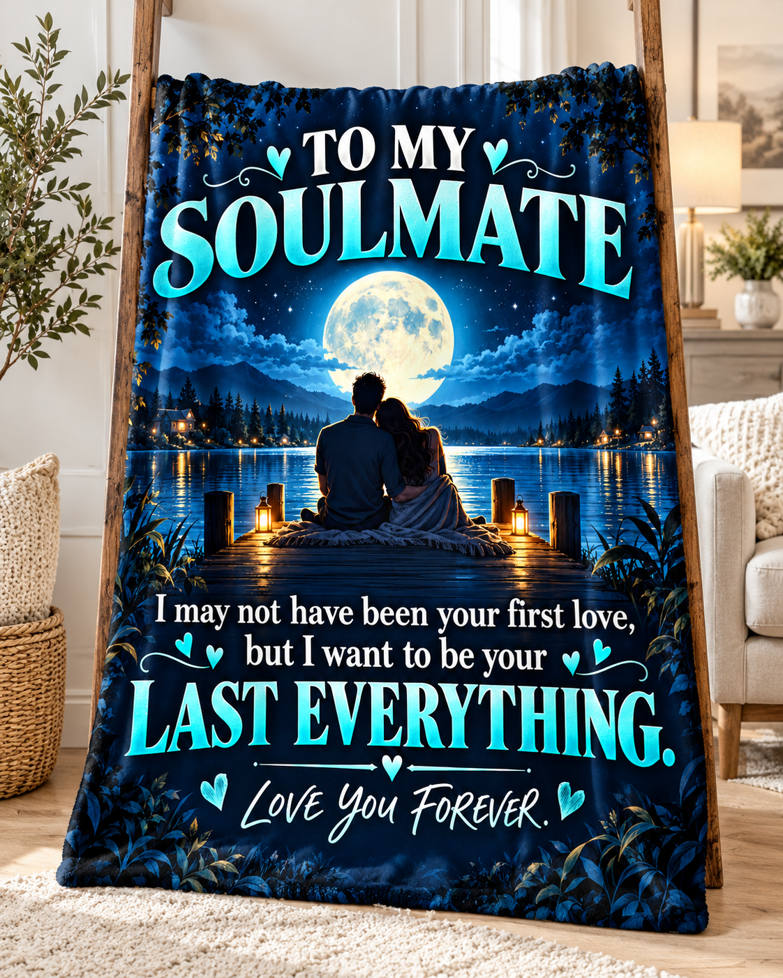 A printed blanket or throw draped over a wooden stand in a living room setting. The design shows a couple sitting on a dock at night by a lake under a full moon, with large teal text reading 'TO MY SOULMATE' and 'I may not have been your first love, but I want to be your LAST EVERYTHING.