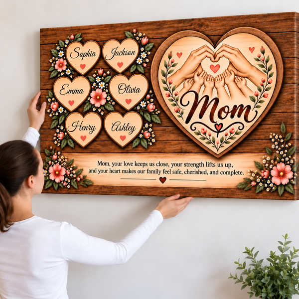 A woman holds a large personalized wooden canvas print against a white wall. The artwork features a heart-shaped design with hands forming a heart, the word 'Mom' in script, six individual heart names with small red hearts, floral details, and a sentimental message for Mom at the bottom.