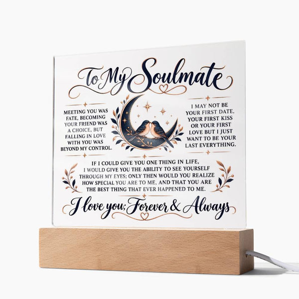 A square white plaque with romantic text and a central illustration of a couple embracing under a crescent moon, displayed on a light wood stand with a power cord visible.