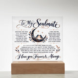 A square white acrylic or glass plaque on a light wood base, featuring romantic text addressed 'To My Soulmate' with a central illustration of a couple under a crescent moon and small floral accents.